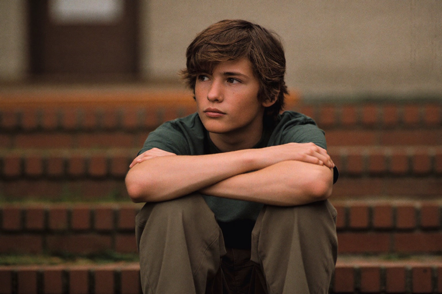 Teen boy sitting alone on outdoor steps, looking into the distance