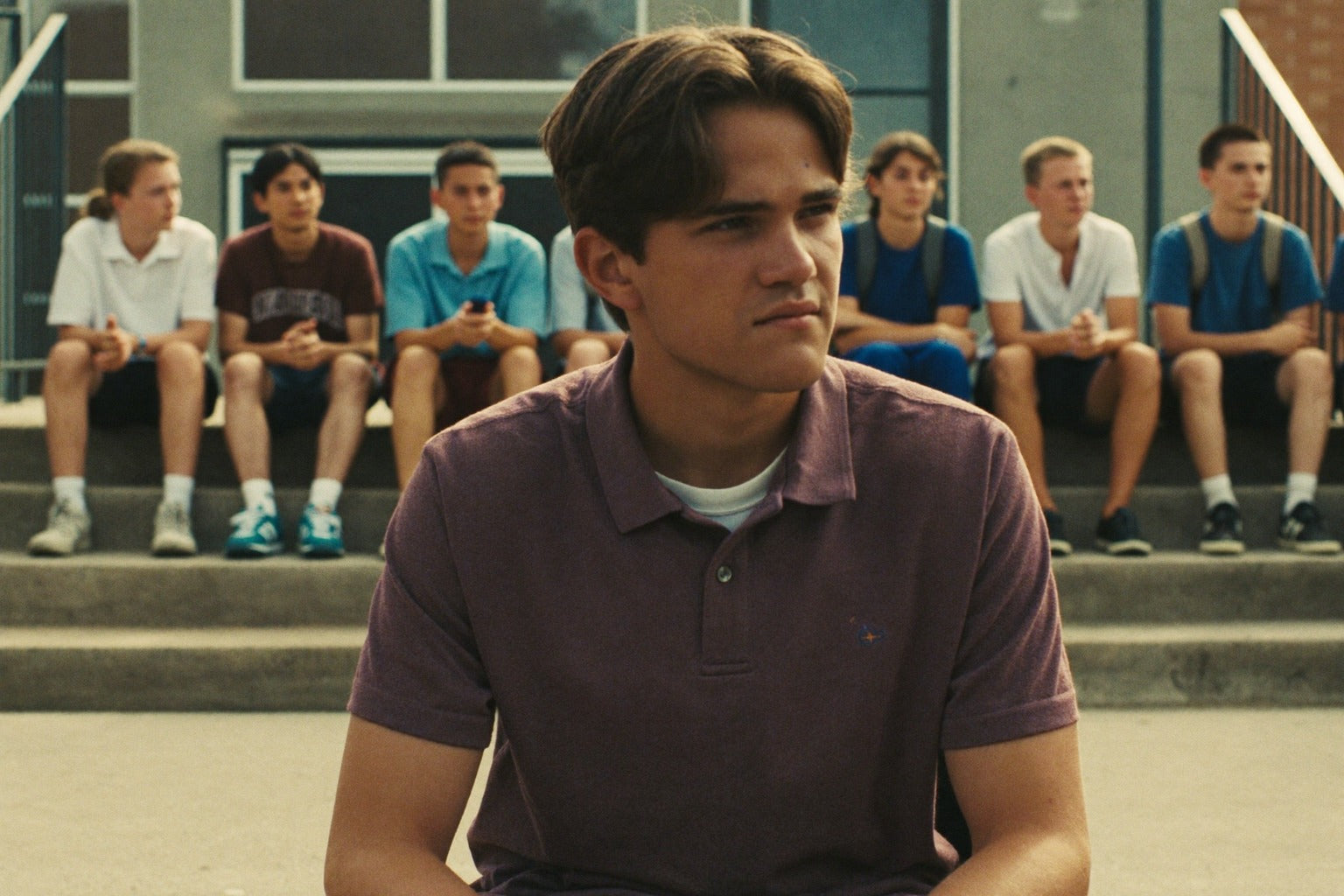 Teen boy sitting alone slightly apart from a group of peers outdoors